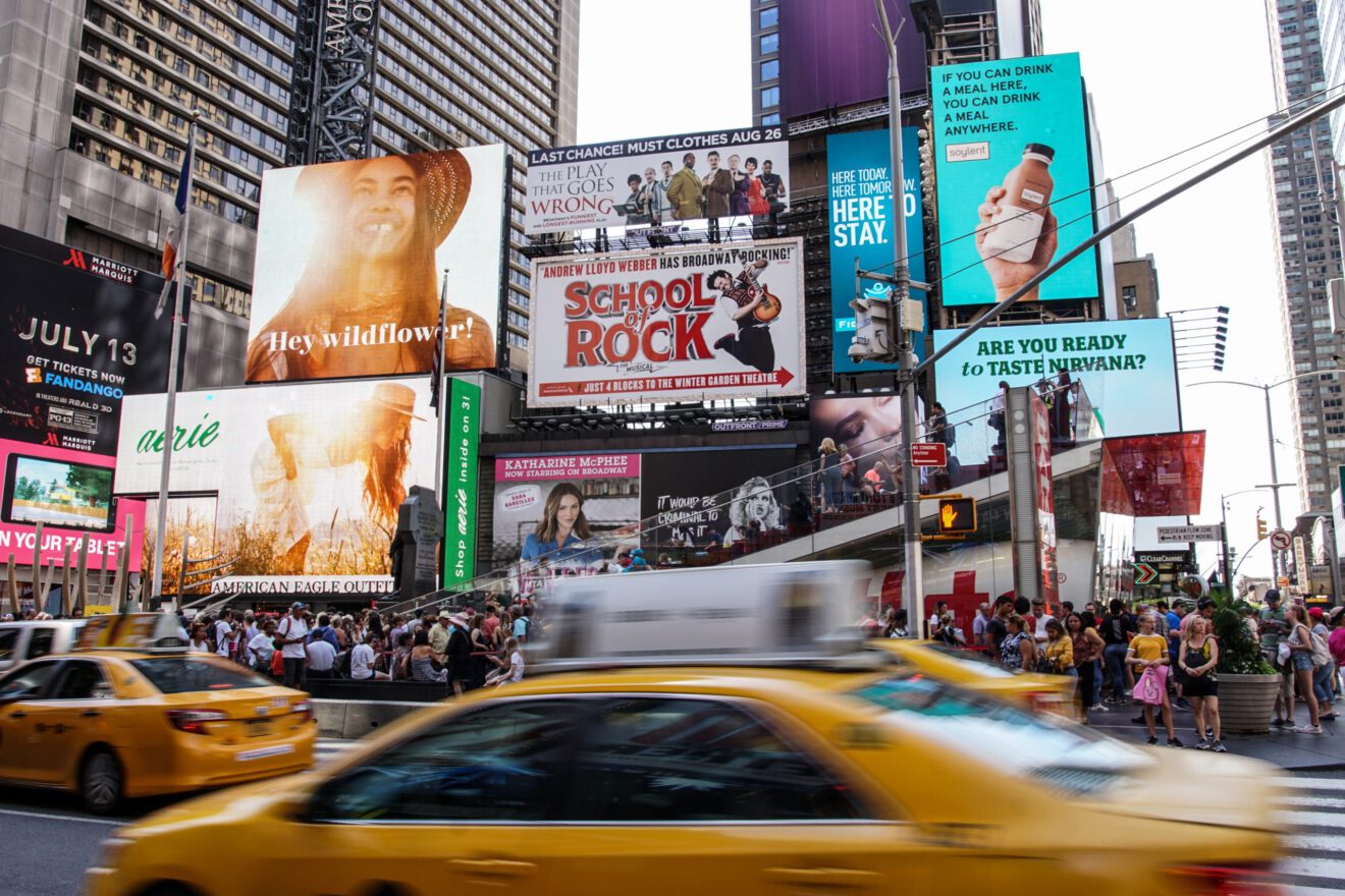 A taxi cab drives past digital billboards.
