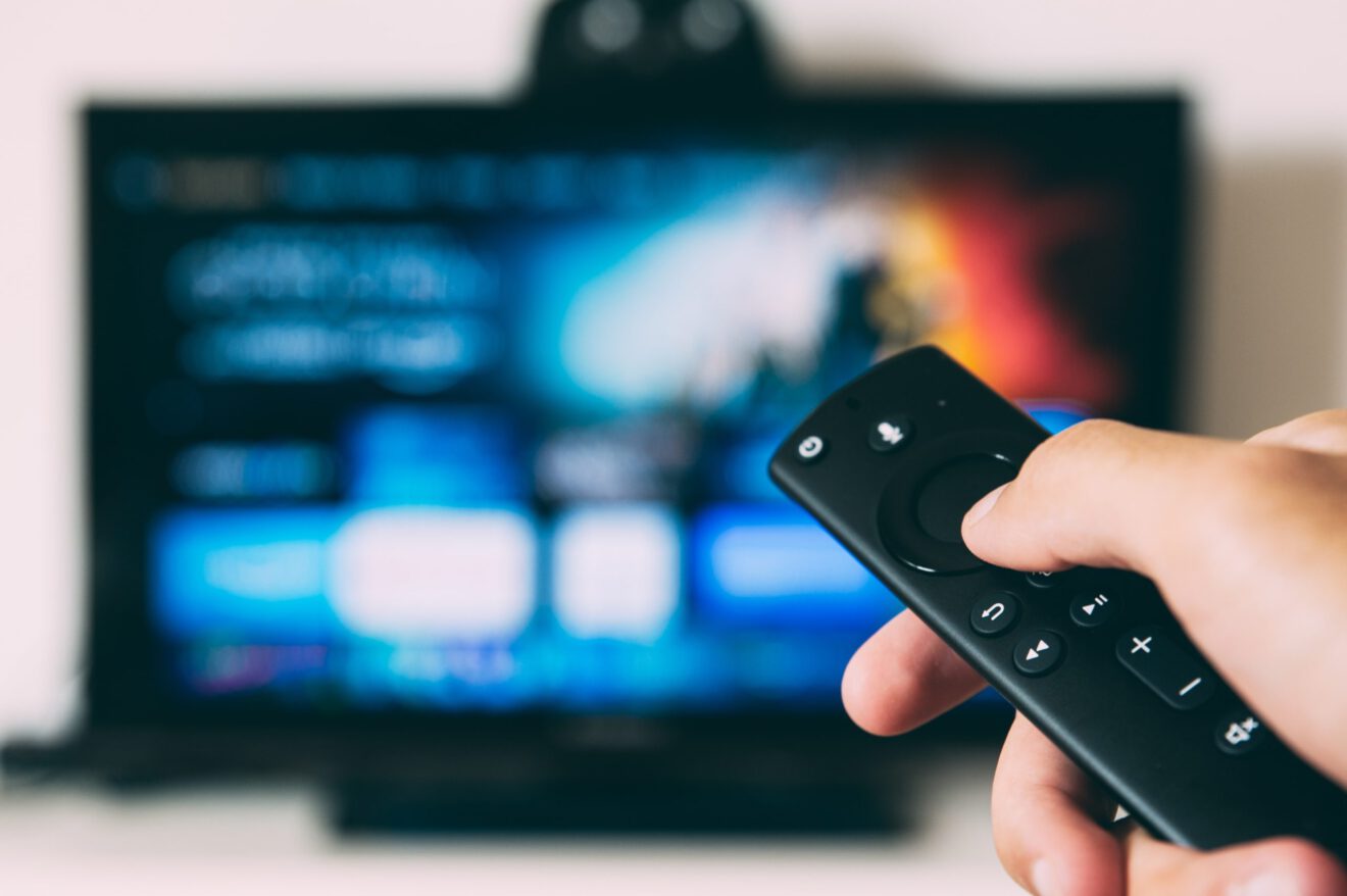 A hand holding a remote control points to a TV with a streaming service on display