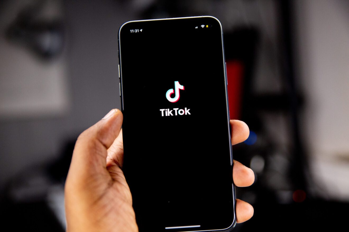 A hand is holding a cell phone that shows the TikTok logo and branding.