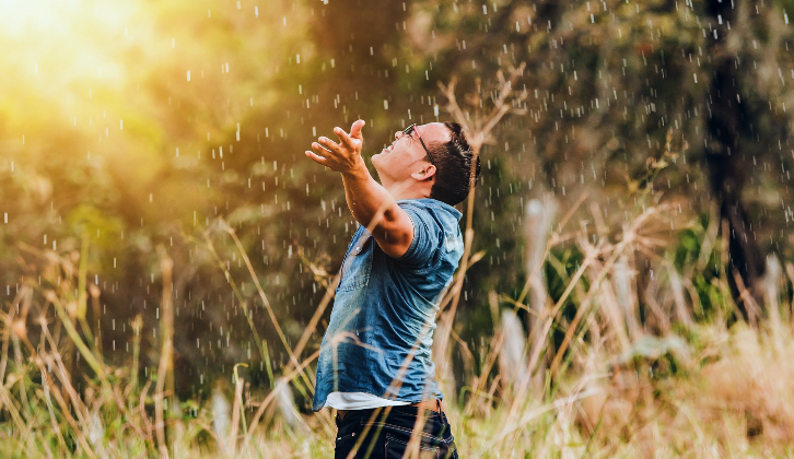 Image of a person in a field, arms raised, to illustrate the earned life