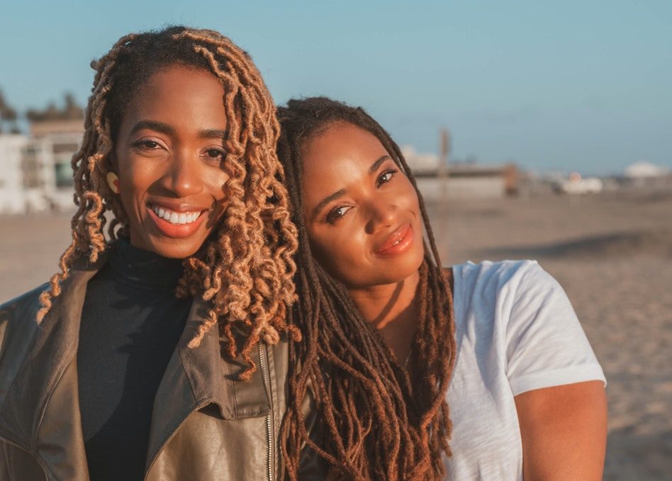 Two Black women smile at the camera.