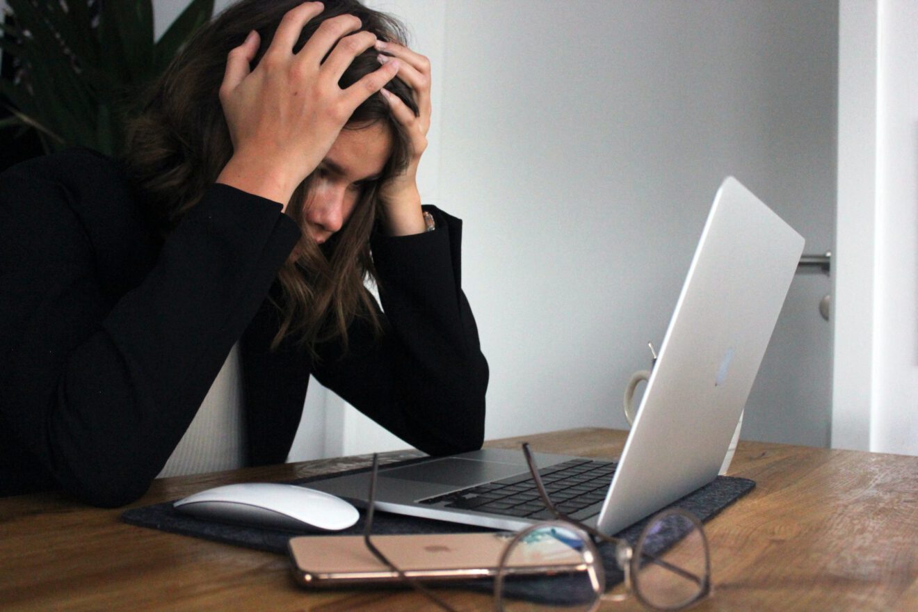 A woman holds her head as she looks at a laptop screen.
