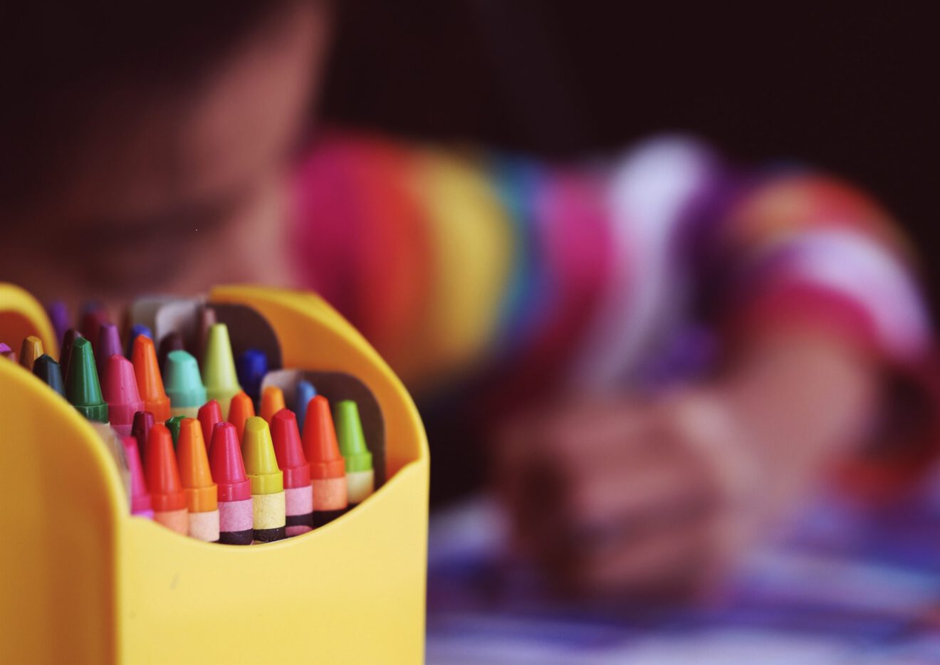 Closeup of box of crayons with blurry child in background for early education article