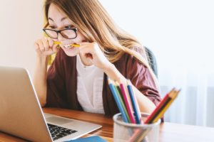 Girl in glasses biting pencil in anxiety while looking at laptop for article on cybersecurity approach