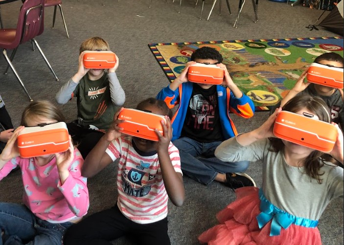 Several elementary-school students from Salem City Schools in Virginia using VR glasses while sitting on the classroom floor.