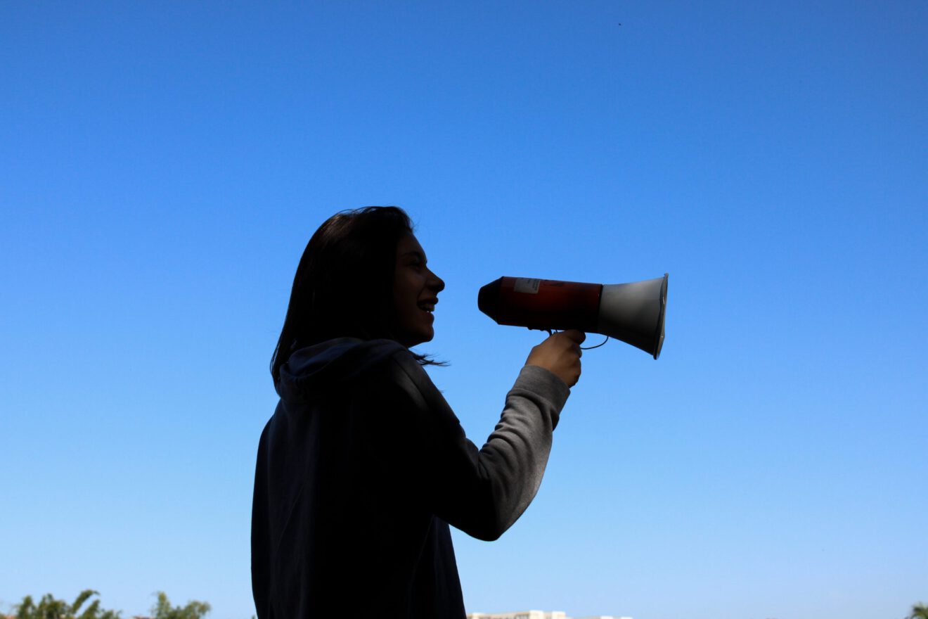 silhouette of woman holding megaphone against blue sky for article on how to consolidate communications in a district