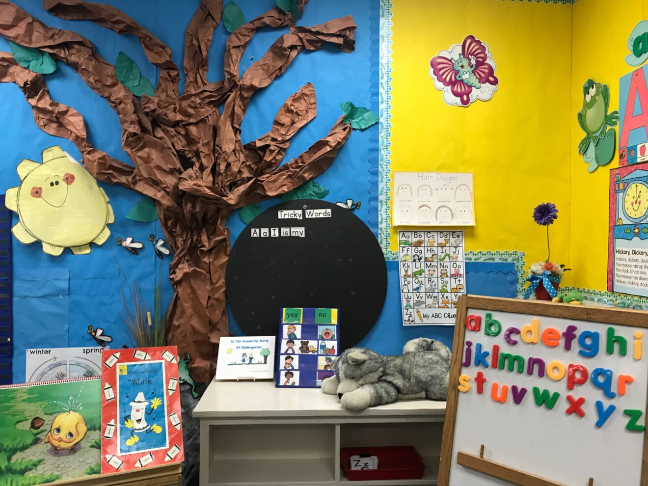 colorful classroom with walls in blue and yellow, with paper tree on wall and lots of activities for article on classroom management