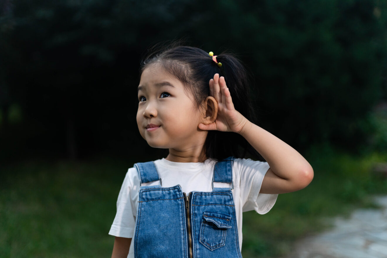 Young girl in denim overalls with hand to her ear for article on instructional audio