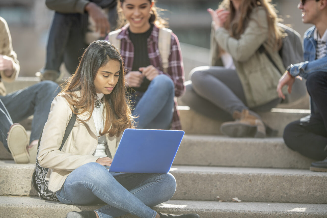 Girl with laptop in foreground sitting on steps of school with other students for article on Horace Mann Award