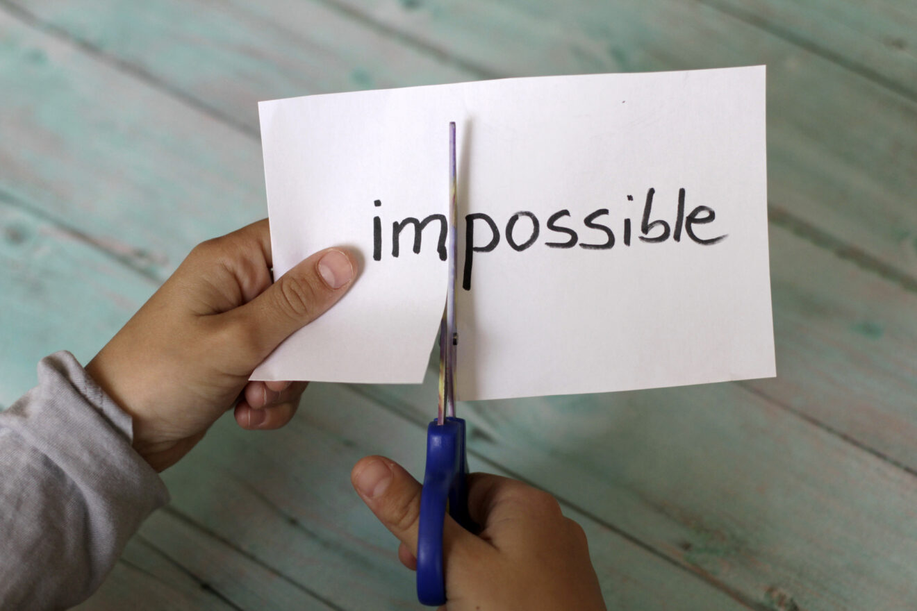 The word impossible written on a white paper, with a hand using scissors to cut the "im" off, for an article on systemic change in schools