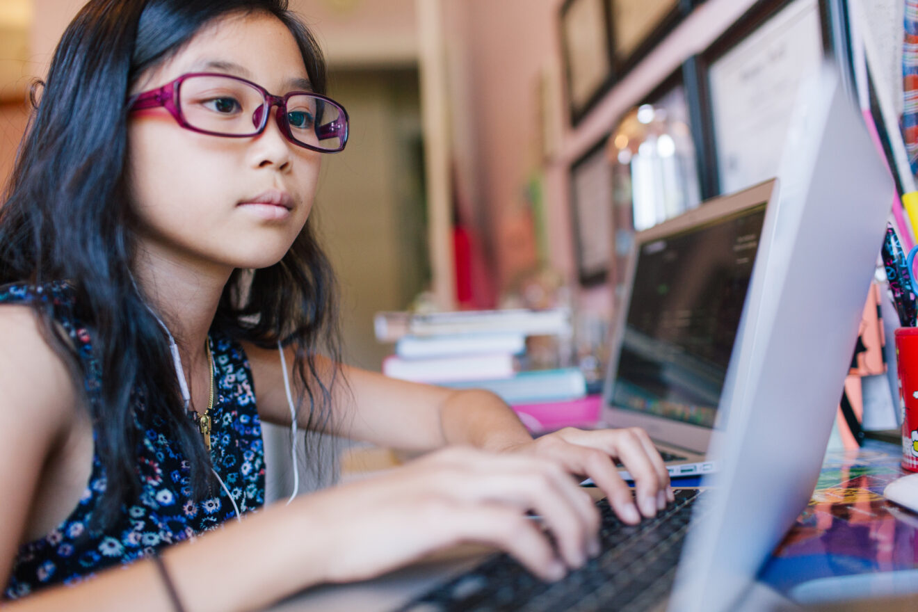 Young girl with glasses typing on laptop on a desk for article on virtual learning