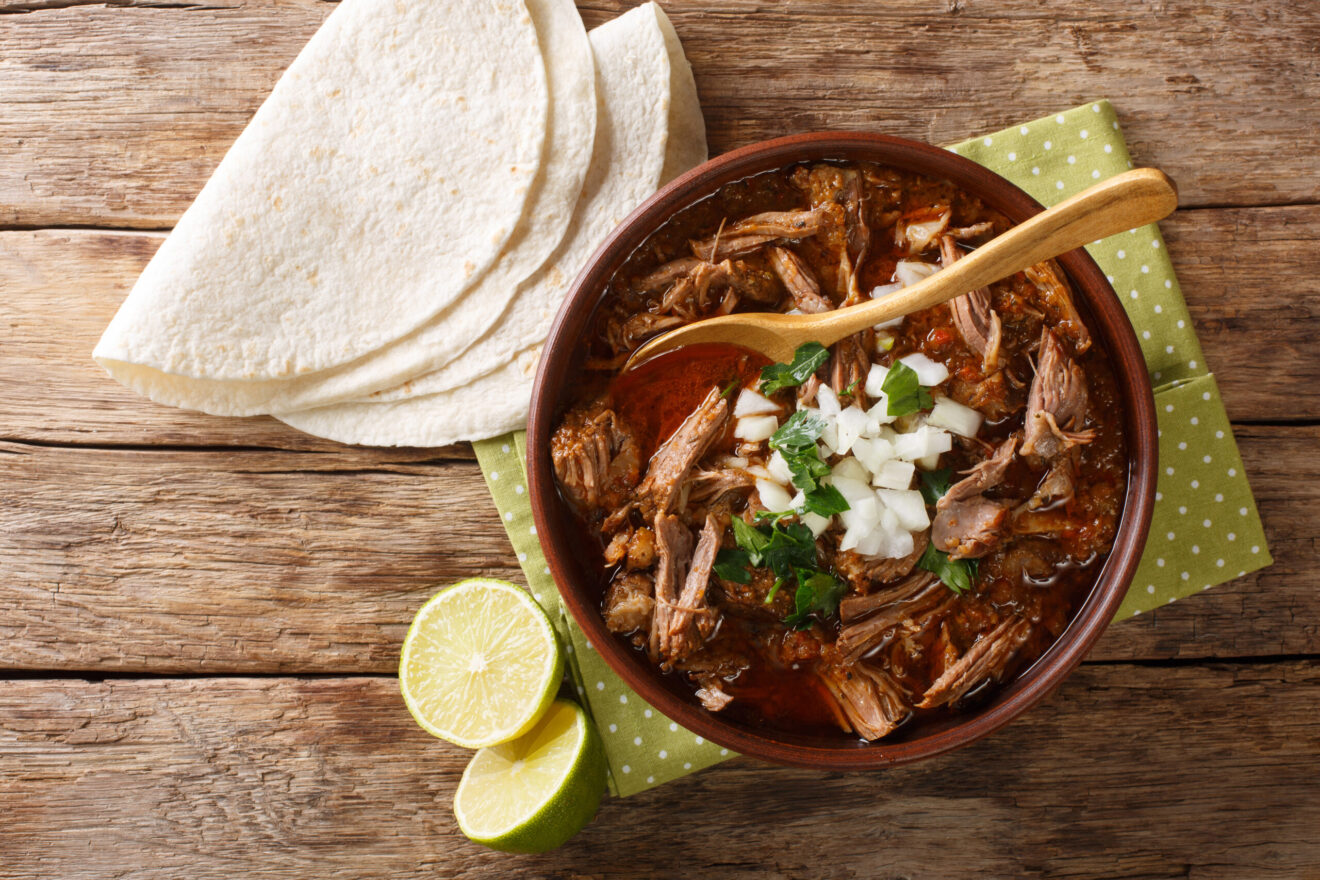 Mexican style slow cooked beef stew Birria de Res served with lime and tortilla closeup in a bowl on the table. Horizontal top view from above