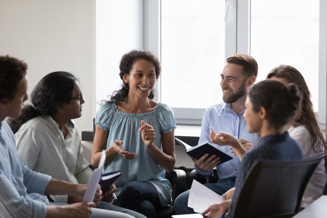 Several diverse adults sitting around in a circle talking in a work environment.