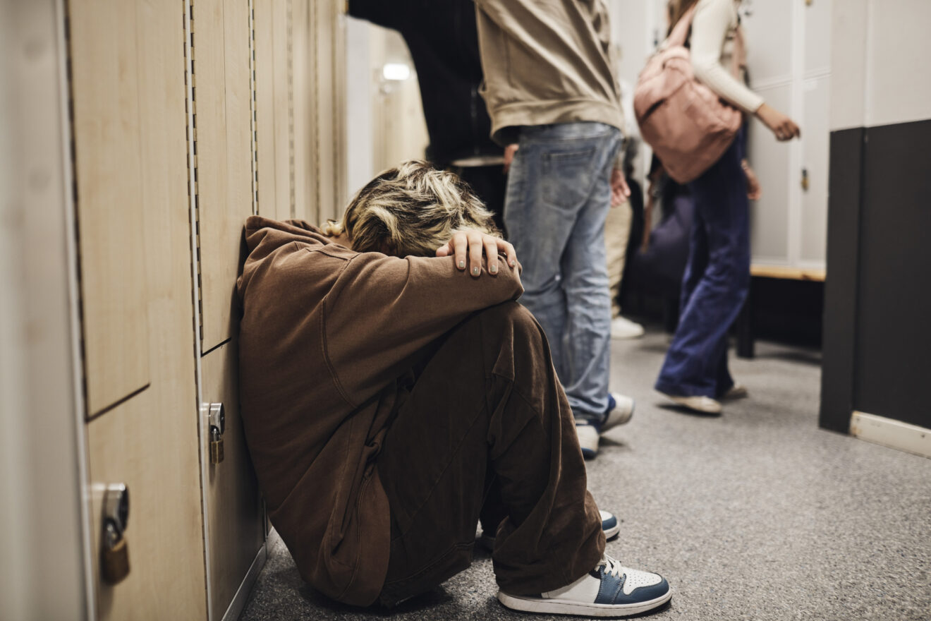 student sitting against school locker with his head buried in his arms on his knees for article on student mental health