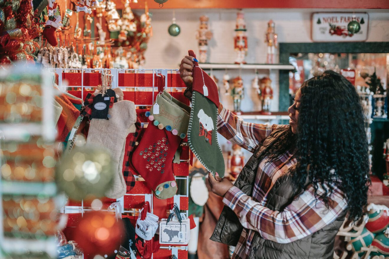 An image of a young Black woman holding up and looking at a Christmas stocking in a retail store.