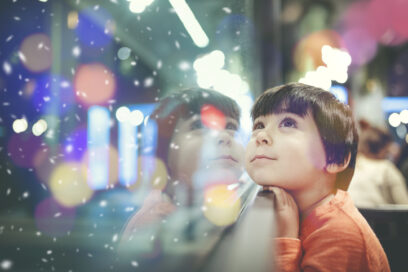 Small child with head against window with multicolored lights and snow, looking out, for article on 1:1 learning