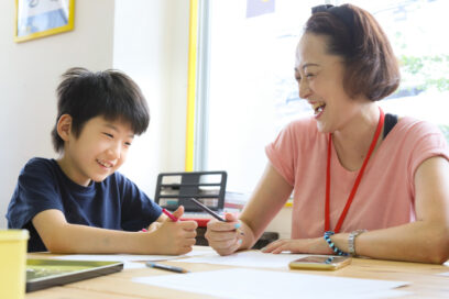 young student and teacher sitting at table with colored pencils drawing on paper and laughing for article on 1:1 learning