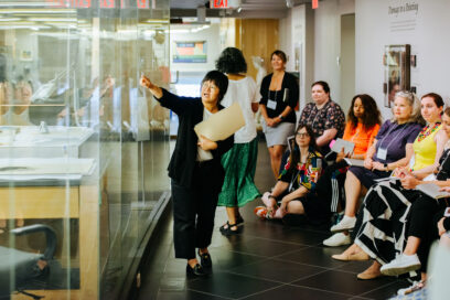 Educator in museum standing in front of glass display case talking to group of seated adults for article on reading portraits.