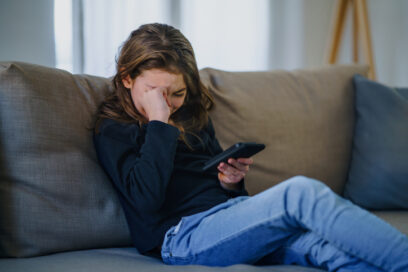 Small girl with smartphone sitting indoors on sofa, crying. for article on social media harm
