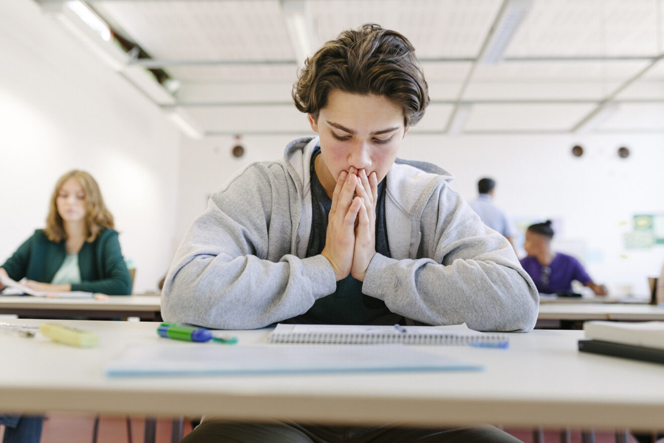 A worried high school student looking at his paper at a classroom table for article on reading for older students.
