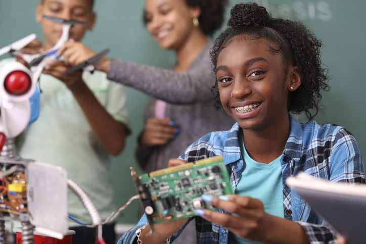 Junior high school age, African American teenage girl works on building a robot in technology class in school classroom setting. STEM topics. article on inclusivity in STEM