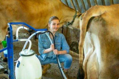 Family organic farm - young female farmer with cows and milking machine for article on career and technical education