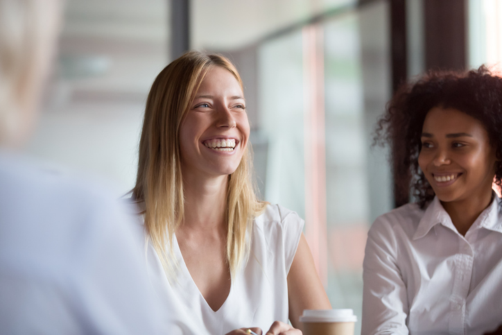 Happy young businesswoman coach mentor leader laughing at funny joke at group business meeting, joyful smiling millennial lady having fun with diverse corporate team people engaged in talking at work for article on teacher coach well-being