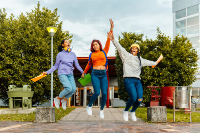 multiracial group of three teenage girls jumping at the exit of the high school. end of exams and classes. beginning of the vacations. for article on instructional coaches year-end activities