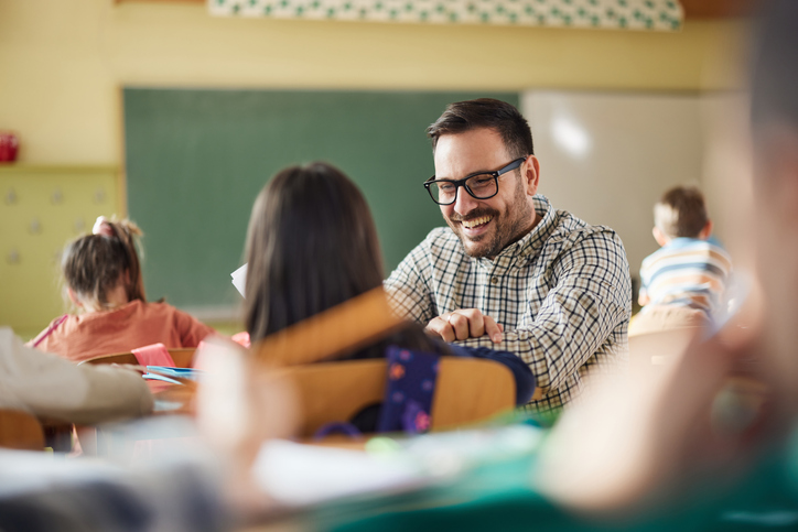 Happy male teacher talking to schoolgirl while assisting her on a class at elementary school. for article on student check-ins