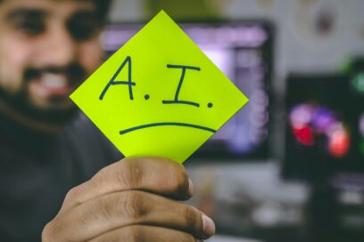 A man behind a computer turning away from it, holding a post-it card with "A.I." on it. Article How generative AI makes scammers alarmingly convincing