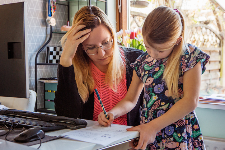 A woman working with a young blonde girl on schoolwork.