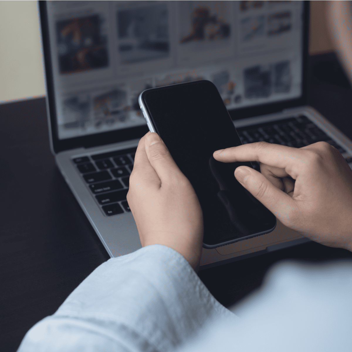 Mobile phone being held up in front of an open laptop with social media images on screen