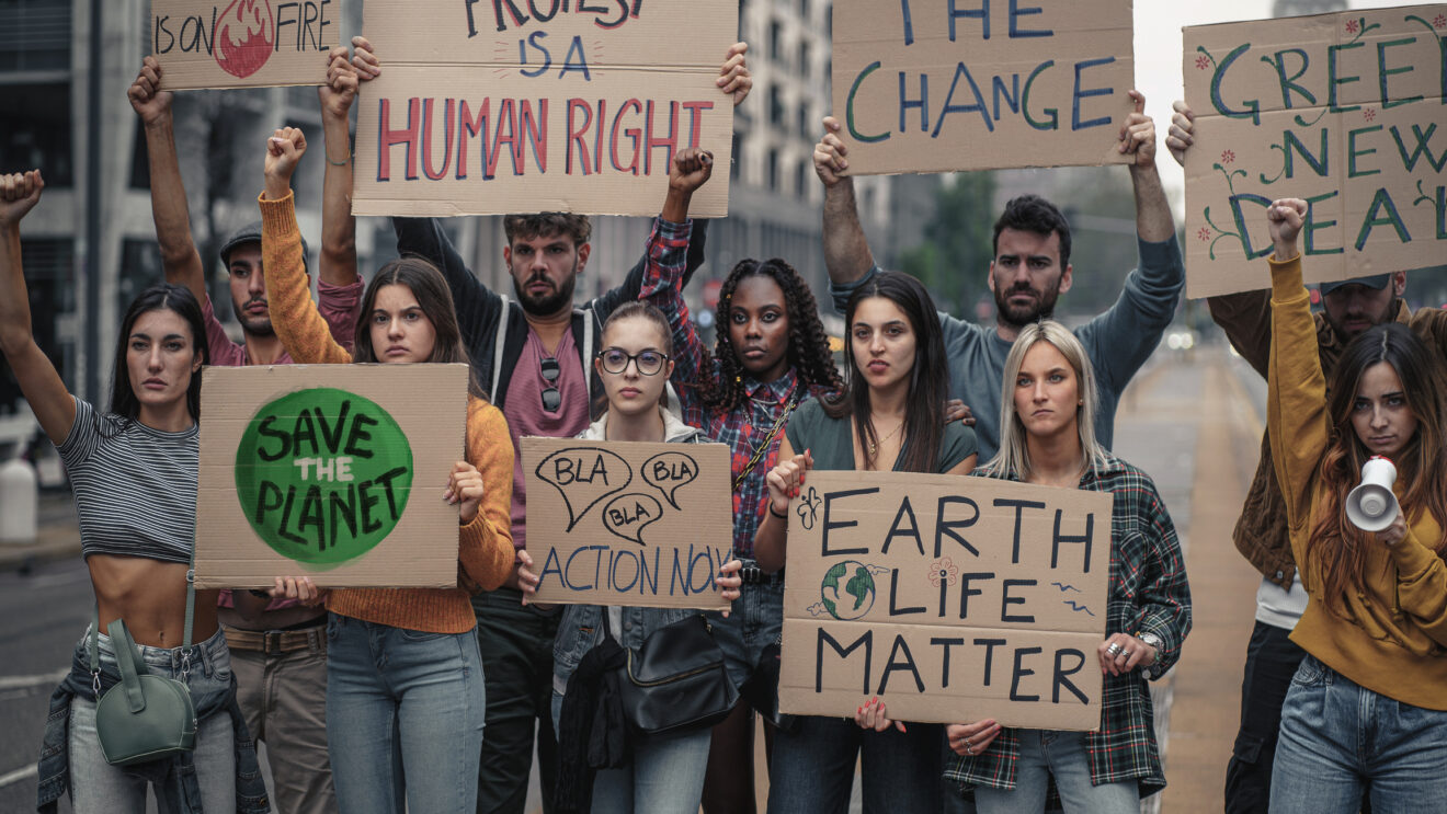 Crowd of young people protesting against climate policy and global warming with raised fists and slogans on placards - concept that illustrates the sensitivity of generation z towards social problems