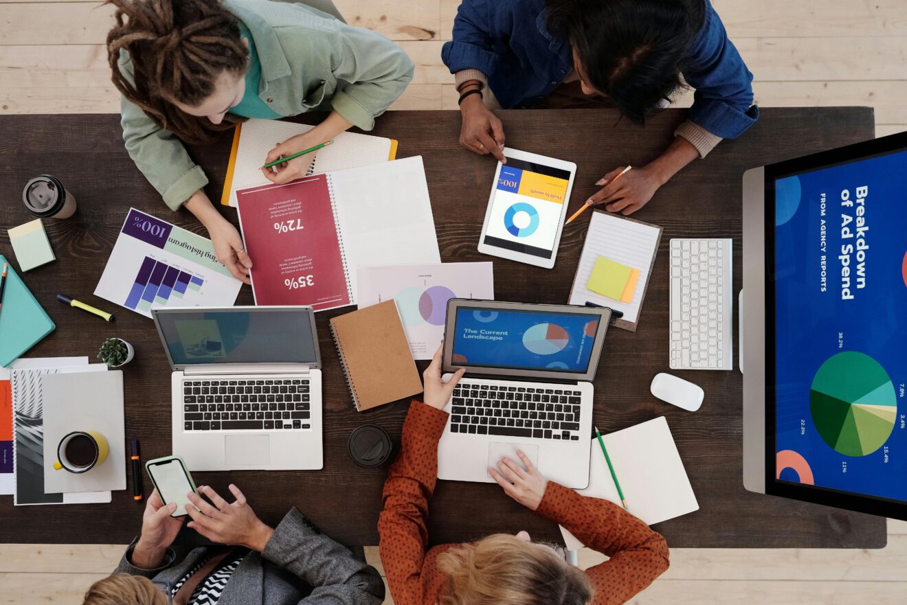 A Group of People Discussing Charts, sitting at a table, with laptops open. Top view