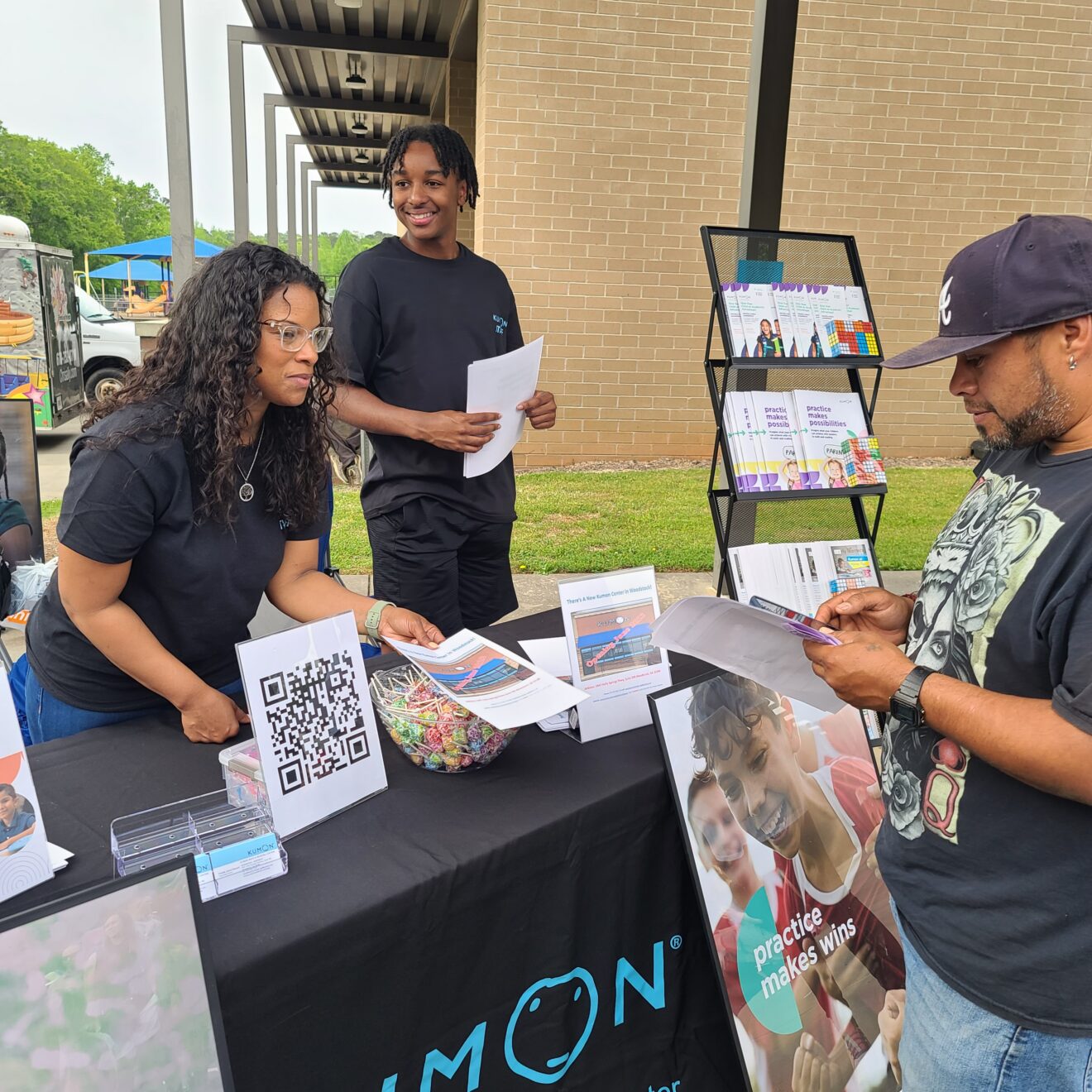 Kumon franchise owner Freeda Jones-Stewart and an older student intteractig with a community member at an information table.