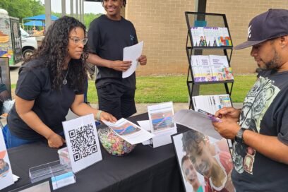 Kumon franchise owner Freeda Jones-Stewart and an older student intteractig with a community member at an information table.