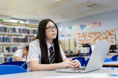 High-school girl with laptop at table, looking pensive