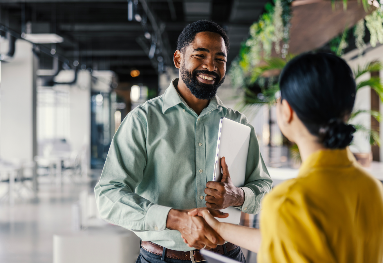 Smiling man holding papers and shaking hands with female in front of him.