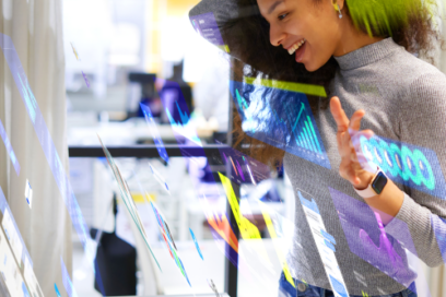 Person smiling while interacting with digital graphics on a transparent display in a modern office.