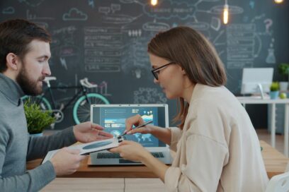 Male on left holding a tablet getting feedback from a female on the right. Both are seated. Used for a SmartBrief Marketing article on how companies can effectively build a marketing team.
