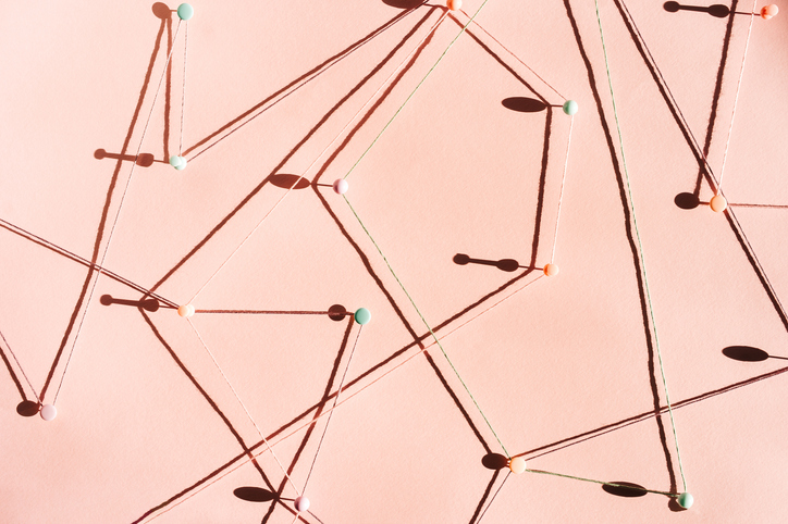 Abstract composition with strings connected by pins on a soft pastel background, forming a geometric web with sharp shadows in natural light. Concept of connection.