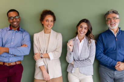 Diverse team of four professional colleagues of different ages and backgrounds looking at the camera in a modern office, representing teamwork, partnership, workplace diversity, and supportive corporate culture.