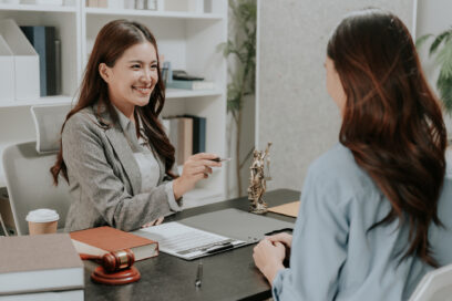 Professional female Asian lawyer holding law book and explaining legal contract details to a stressed client in corporate law firm office.